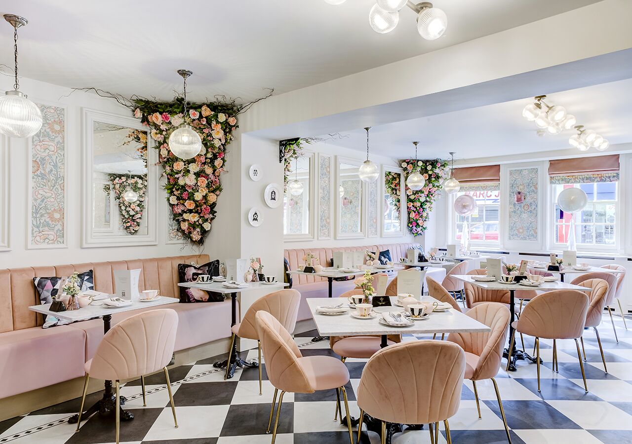A chic cafe with pink and white decor, featuring a checkered floor, floral wall decorations, and modern lighting.