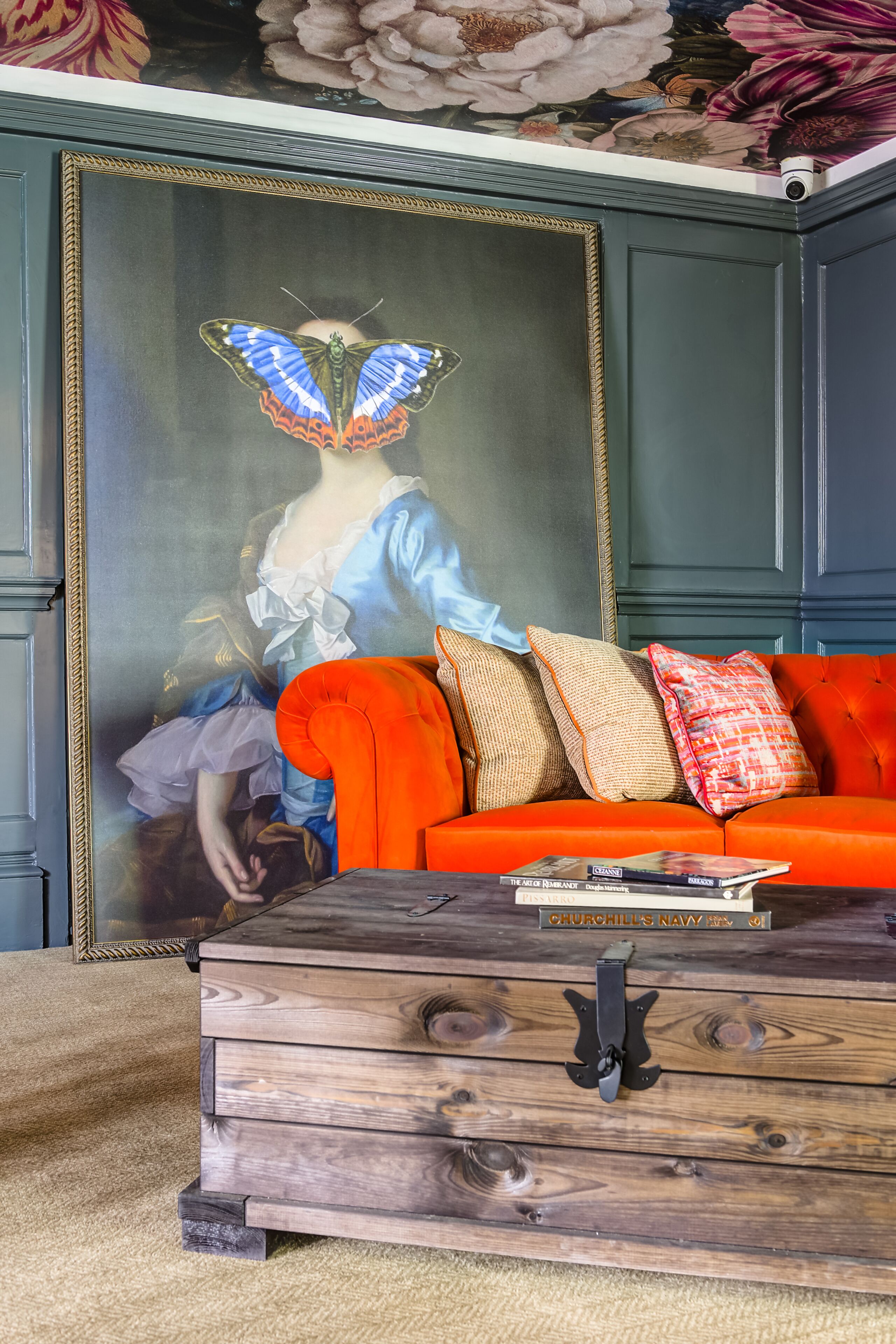 A room with a large framed painting, a red sofa, and a wooden chest of drawers.