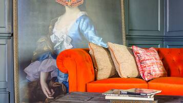 A room with a large framed painting, a red sofa, and a wooden chest of drawers.