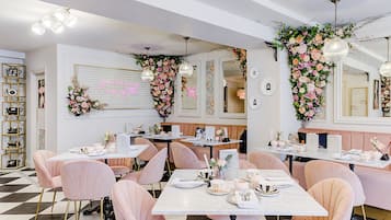 Un restaurant avec des chaises roses, des tables blanches et une décoration florale.