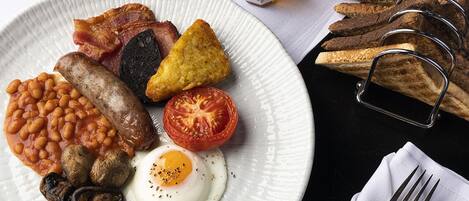 Un plato de desayuno con tocino, salchichas, frijoles, champiñones, un huevo frito y tomate.