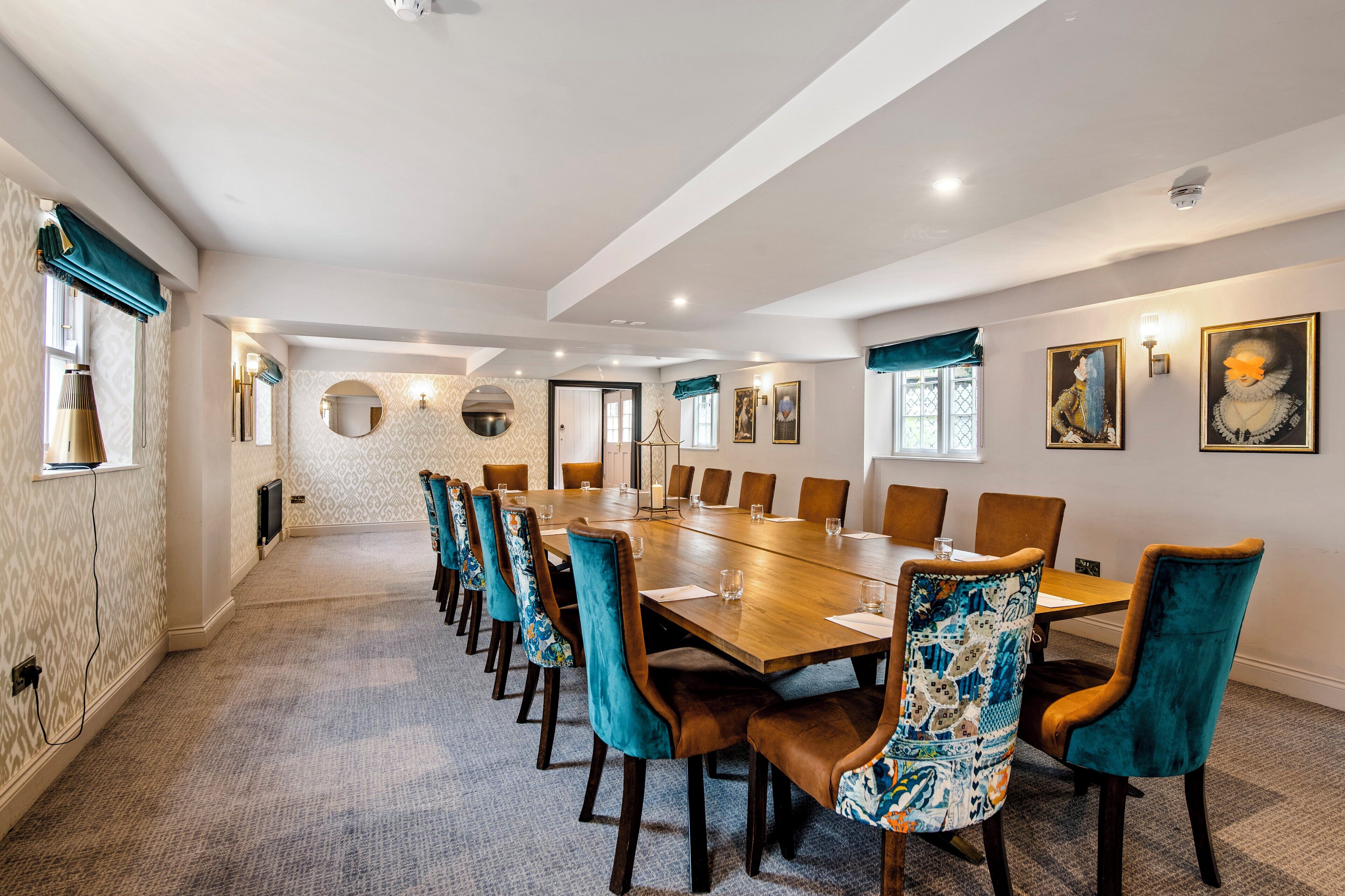 A conference room with a long table, teal upholstered chairs, and framed artwork on the walls.