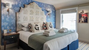 A neatly made bed with a decorative headboard, two bedside lamps, and a window with a view of the city.