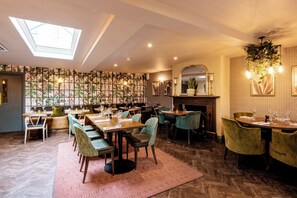 A restaurant with high ceilings, a skylight, patterned wallpaper, and a mix of wooden and upholstered furniture. - The George of Colchester (Colchester)