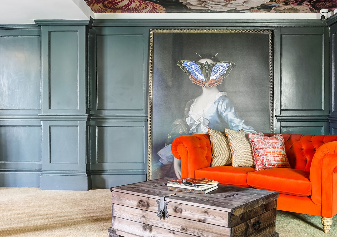 A room with a dark green paneled wall, a red sofa with patterned cushions, and a wooden coffee table with books.