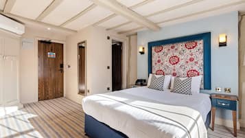 Una habitación de hotel con una cama grande, cabecera con diseño estampado, mesita de noche con lámpara y puerta con un cartel.