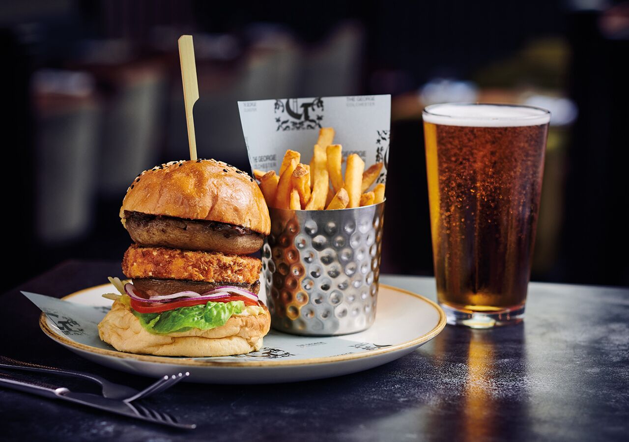 Una hamburguesa con papas fritas y un vaso de cerveza sobre una mesa.