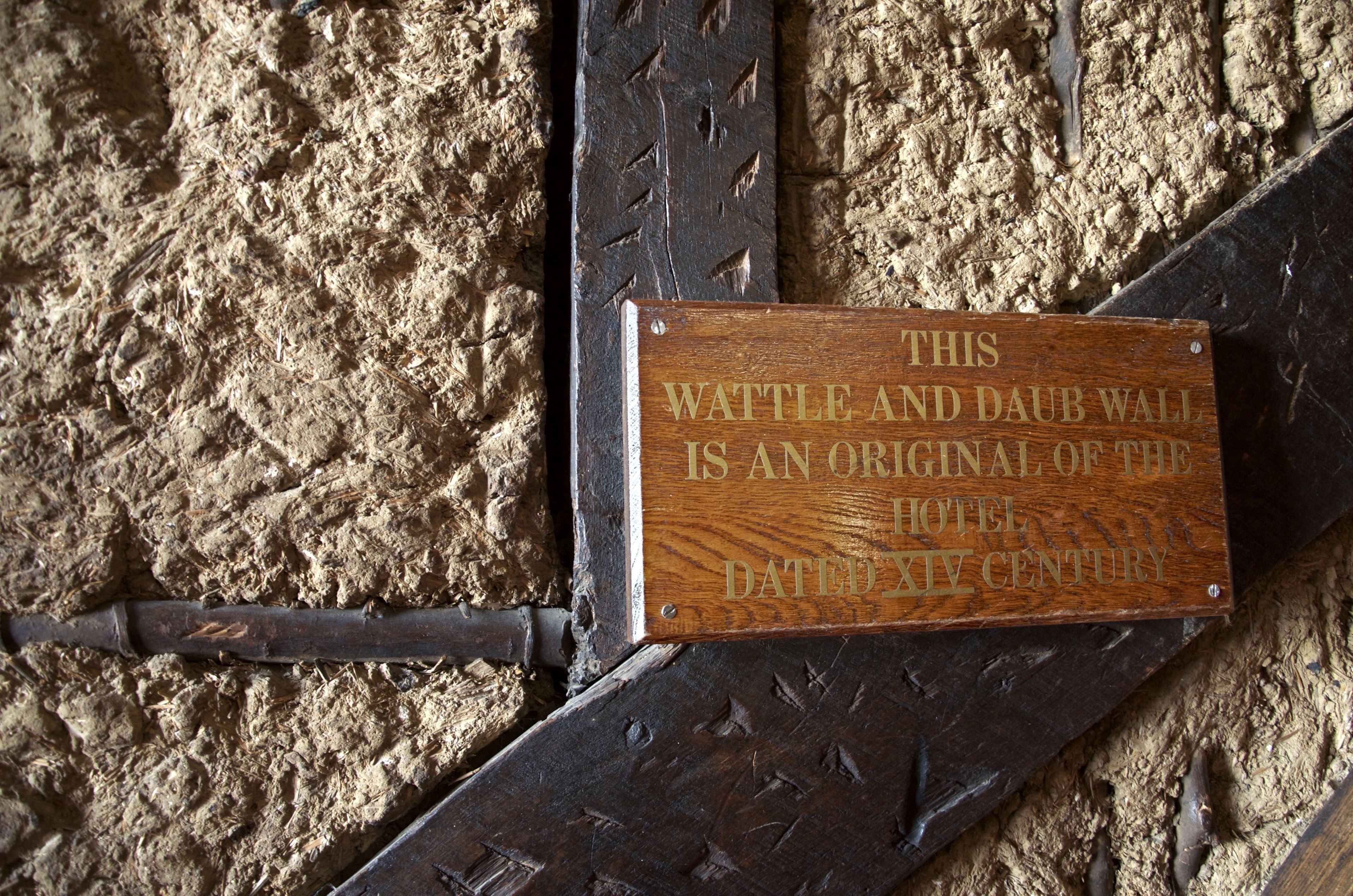 A wooden plaque on a textured wall with a metal frame, stating the wall is an original of the hotel dated 14th century.