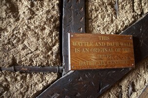 Una placa de madera en una pared texturizada con marco de metal, que indica que la pared es original del hotel y data del siglo XIV.