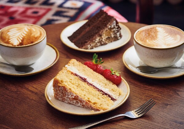 A table with a slice of cake, two cups of coffee, and a fork. - The George of Colchester (Colchester)