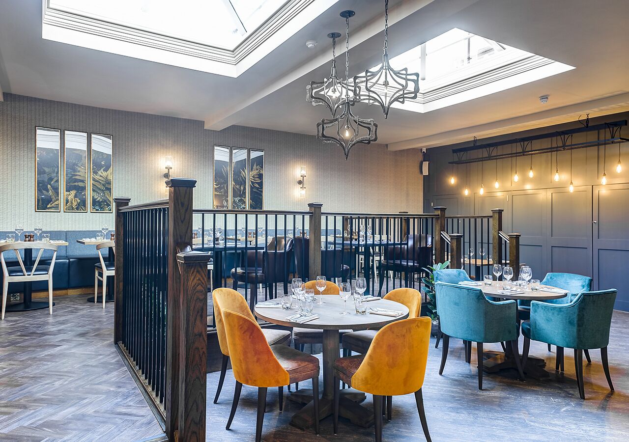 A restaurant with round tables, blue and yellow chairs, and a high ceiling with skylights.