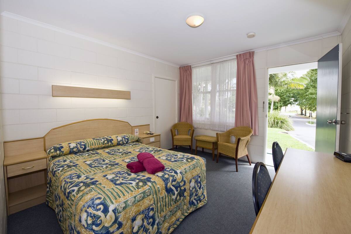 A hotel room with a bed, a desk, two chairs, and a view of the outdoors.