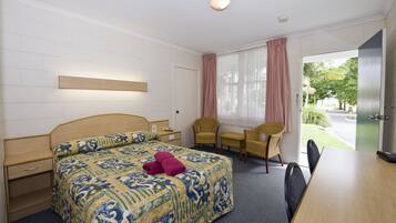 A hotel room with a bed, a desk, two chairs, and a view of the outdoors.