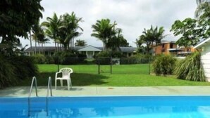 A swimming pool with a white chair and a grassy area with palm trees. - Colonial Court Motor Inn (Kempsey)