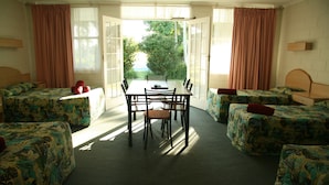 A room with a dining table and four single beds with floral bedding. - Colonial Court Motor Inn (Kempsey)