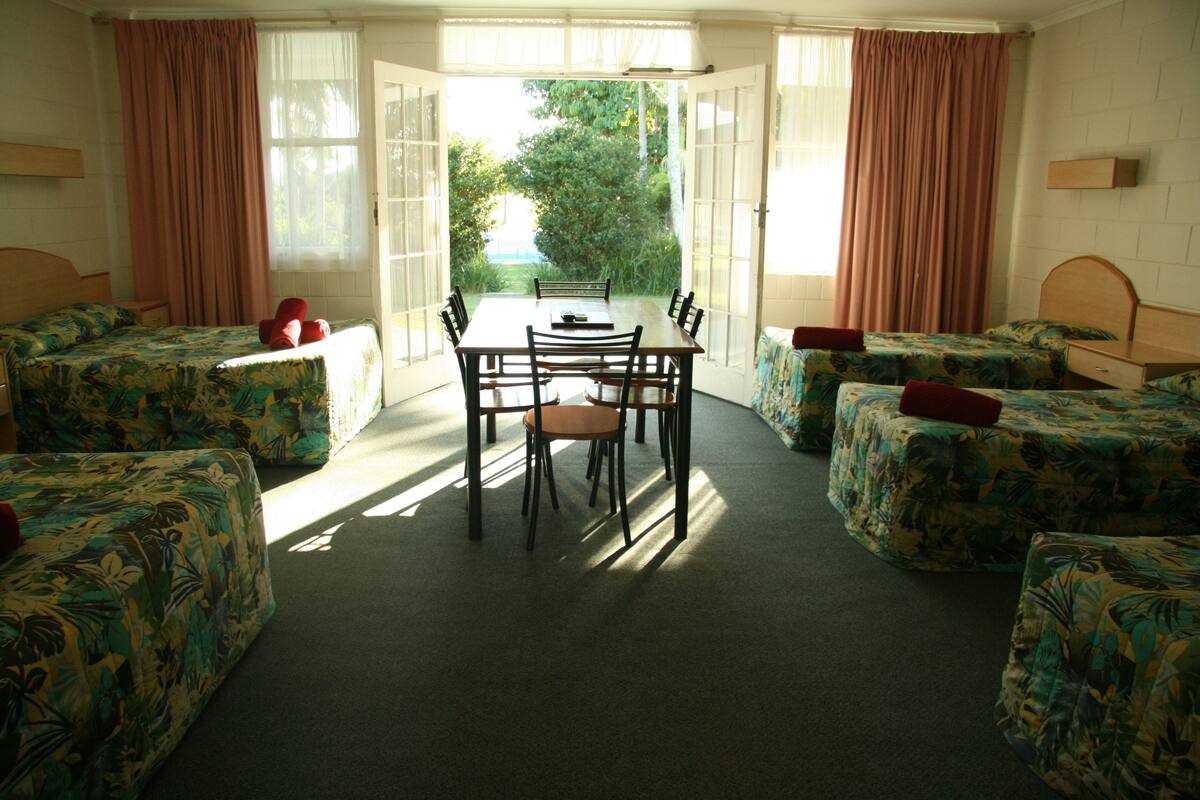 A room with a dining table and four single beds with floral bedding.