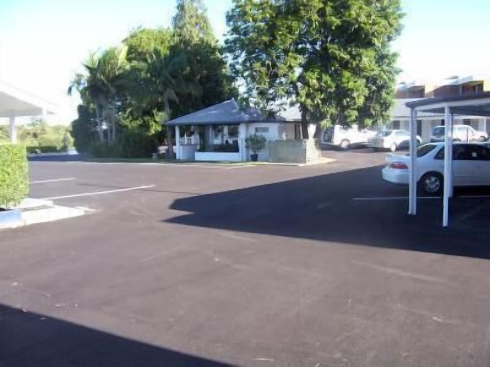 A parking lot with a covered car parking area, a small building, and trees in the background.