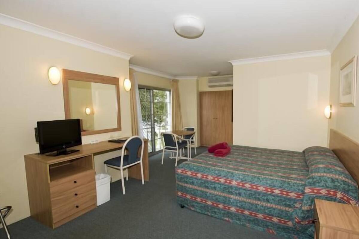 A hotel room with a bed, a desk with a computer, a chair, and a television.