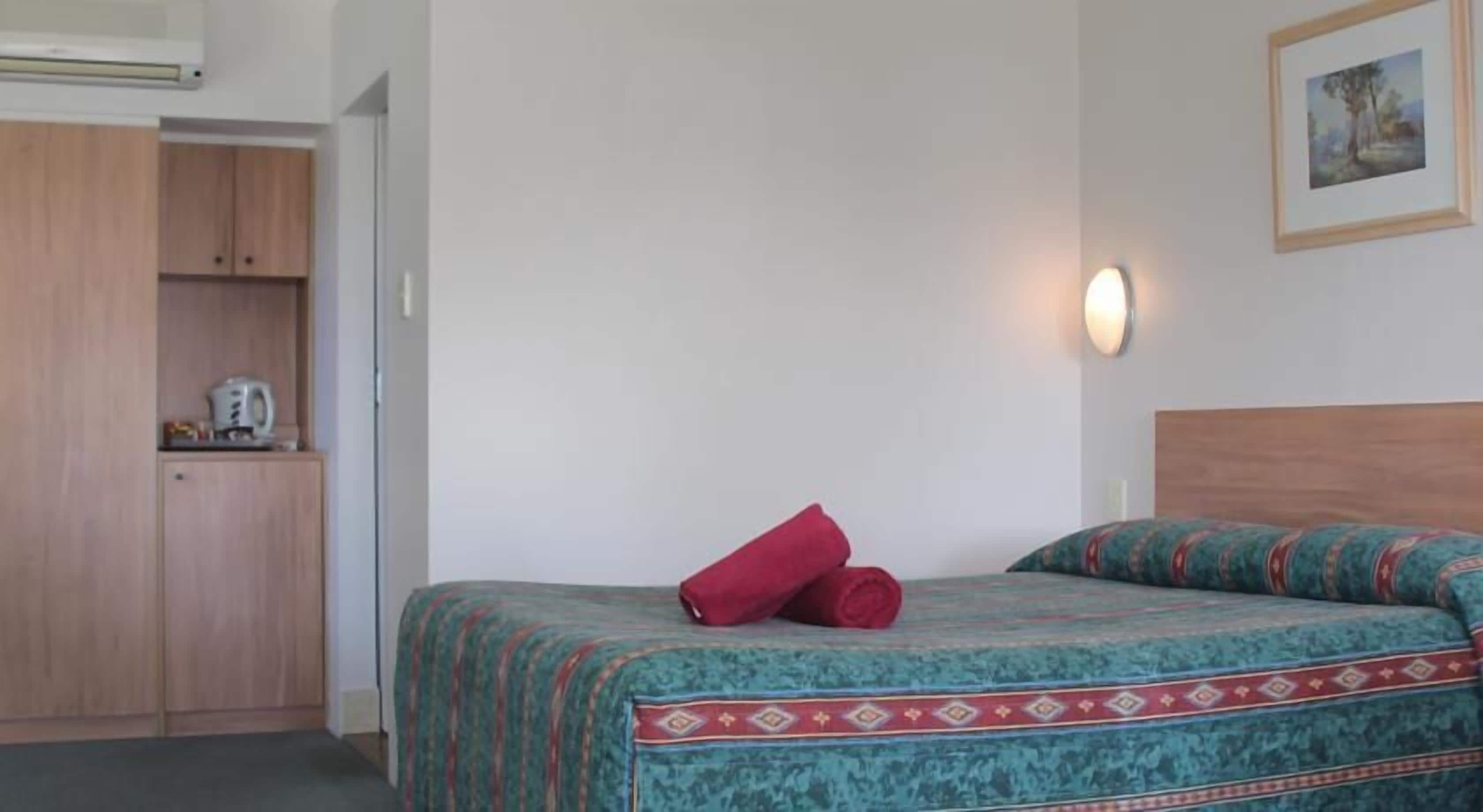 Un dormitorio con cama, mesita de noche, armario y un cuadro en la pared.