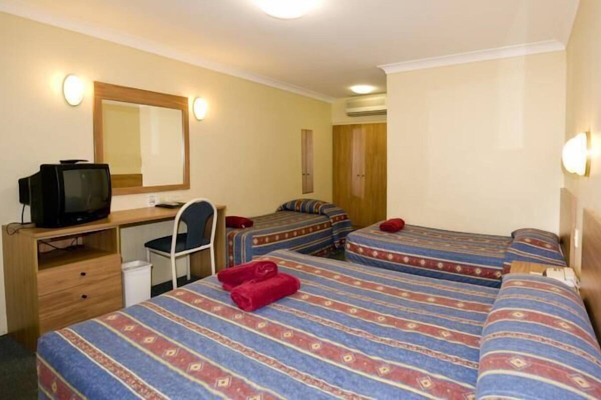 A hotel room with two beds, a desk with a television, a chair, and a mirror.