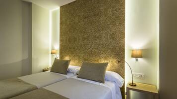 A hotel room with two beds, a patterned wall, and bedside lamps.