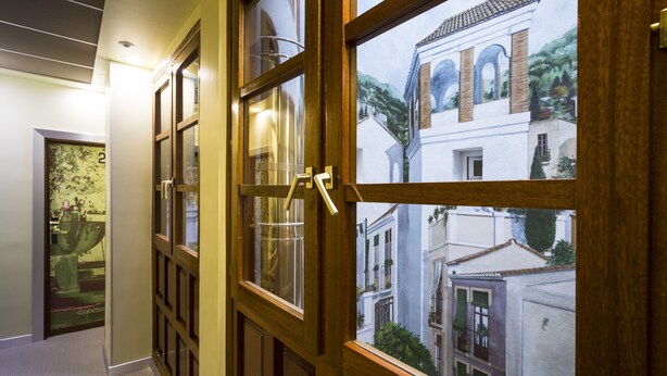 A hallway with wooden doors and windows, leading to a view of buildings outside. - Hotel Comfort Dauro 2 (Granada)
