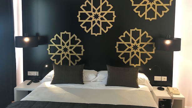 Una habitación de hotel con cama, mesitas de noche, lámparas y paneles decorativos en la pared.