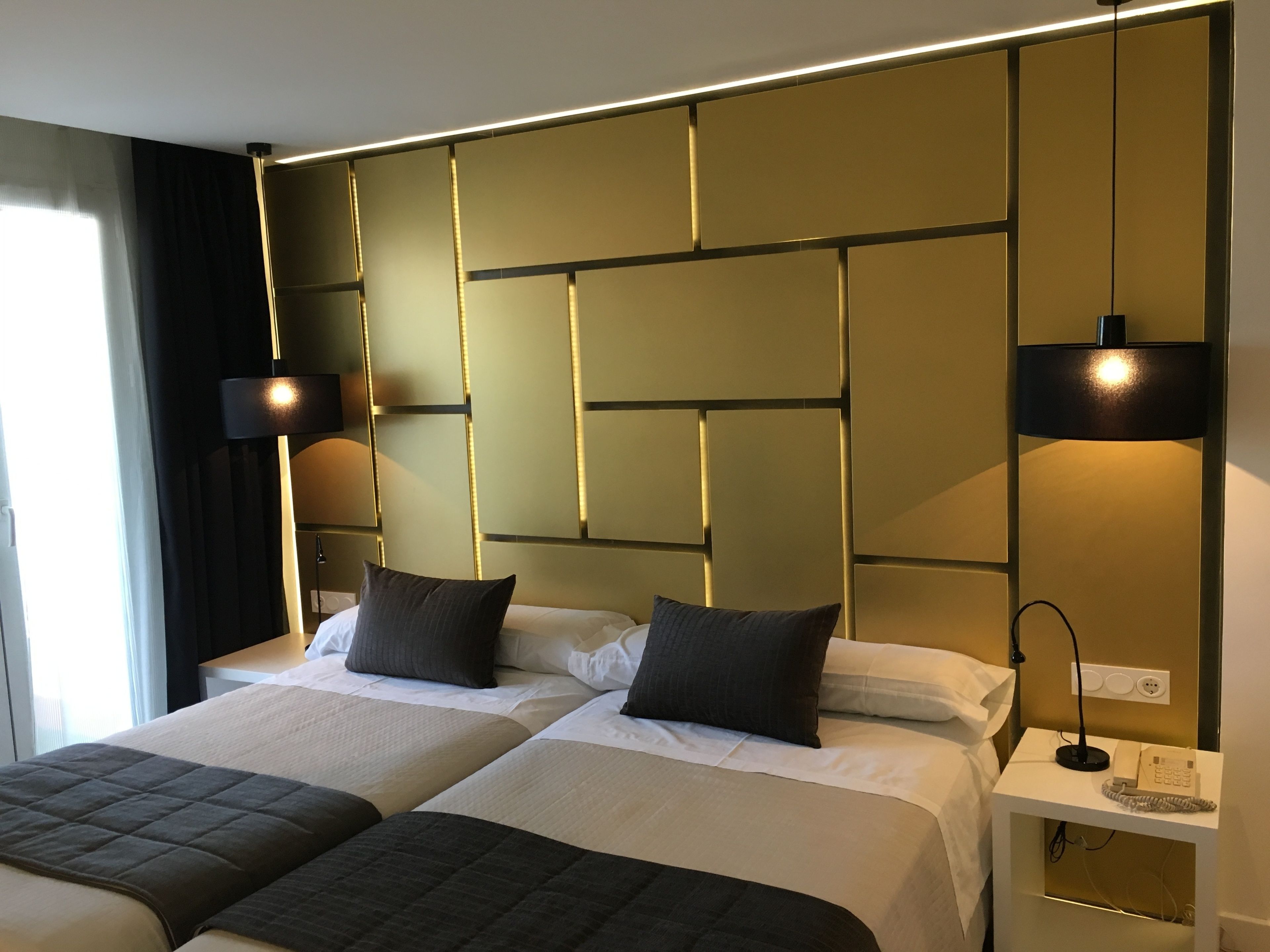 A hotel room with two beds, a bedside table with a telephone, and a wall-mounted light fixture.