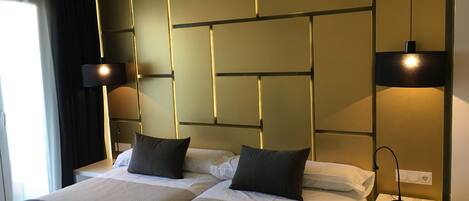 A hotel room with two beds, a bedside table with a telephone, and a wall-mounted light fixture.