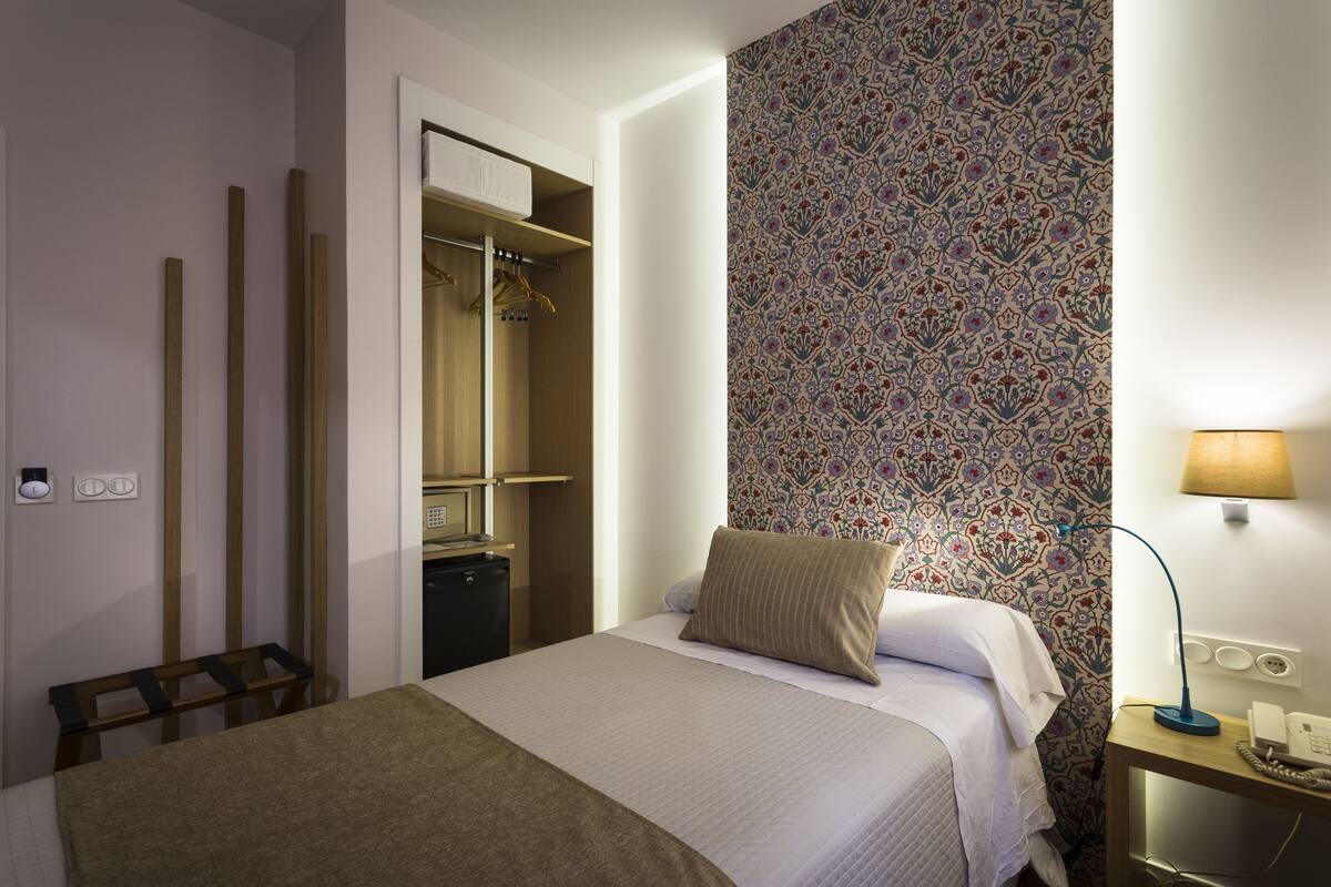 Una habitación de hotel con cama, mesita de noche, lámpara y armario.