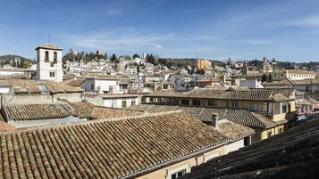A cityscape with terracotta-tiled rooftops, a prominent bell tower, and a mix of historical and modern buildings.