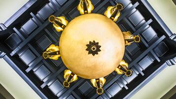 A central, round, gold-colored fixture with a star emblem, surrounded by eight gold-colored, flower-shaped elements, set against a black, grid-patterned background.