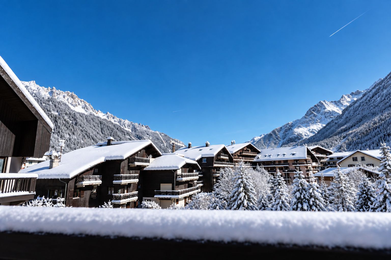 Un ensemble de chalets en bois dotés de balcons, se dressant sur un fond de montagnes enneigées et d’un ciel d’un bleu éclatant.