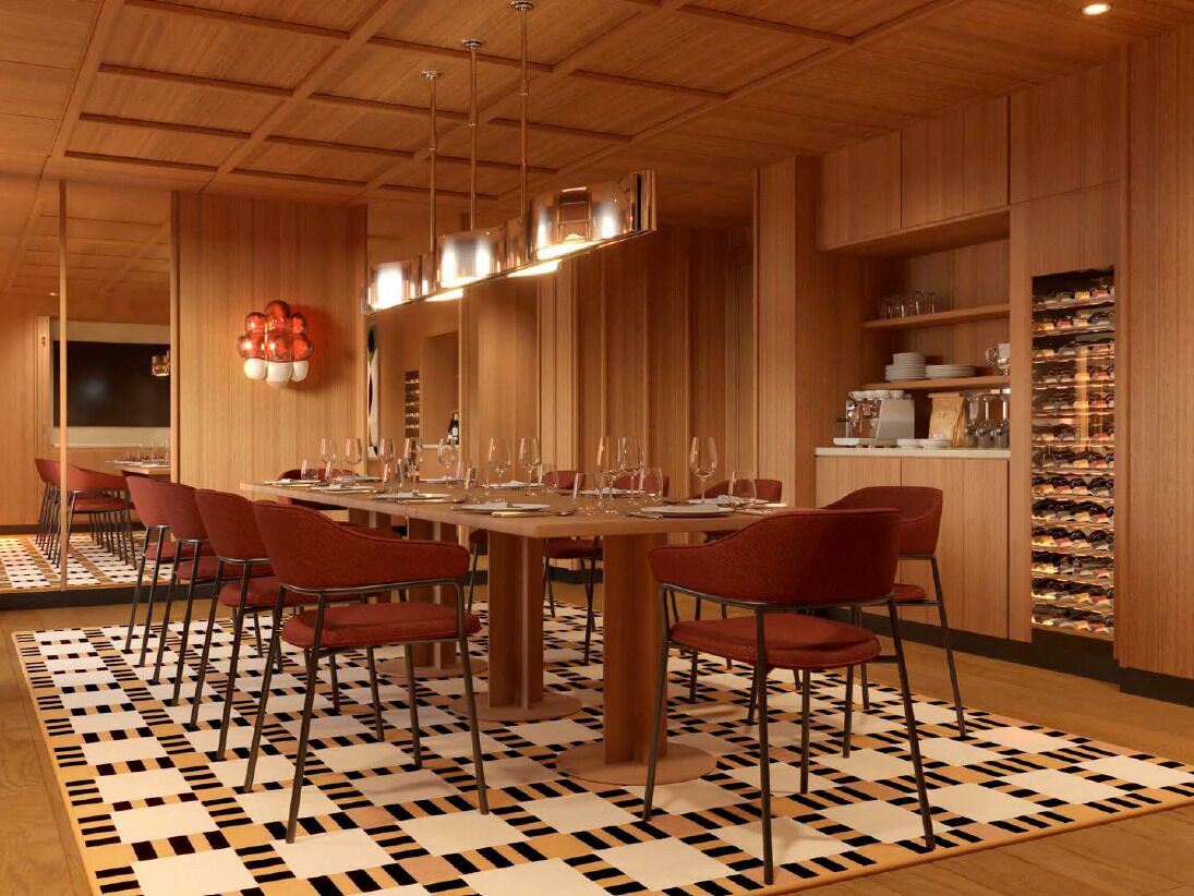 Un espace repas avec une longue table, des chaises rouges et un sol à motifs.