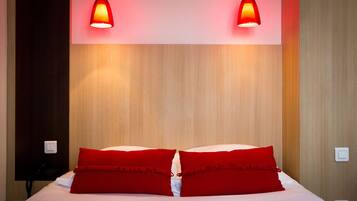 Habitación de hotel con una cama, dos almohadas rojas, un cabecero de madera y dos lámparas colgantes.
