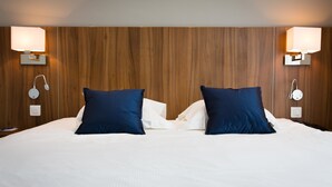 Une chambre d’hôtel avec un grand lit, deux oreillers bleus, du linge de lit blanc et des lampes fixées au mur.