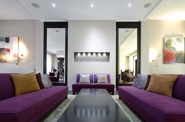 A modern living room with two purple sofas, a central coffee table, and a decorative wall piece. - Best Western Plus Hotel Plaisance (Villefranche-sur-Saône)