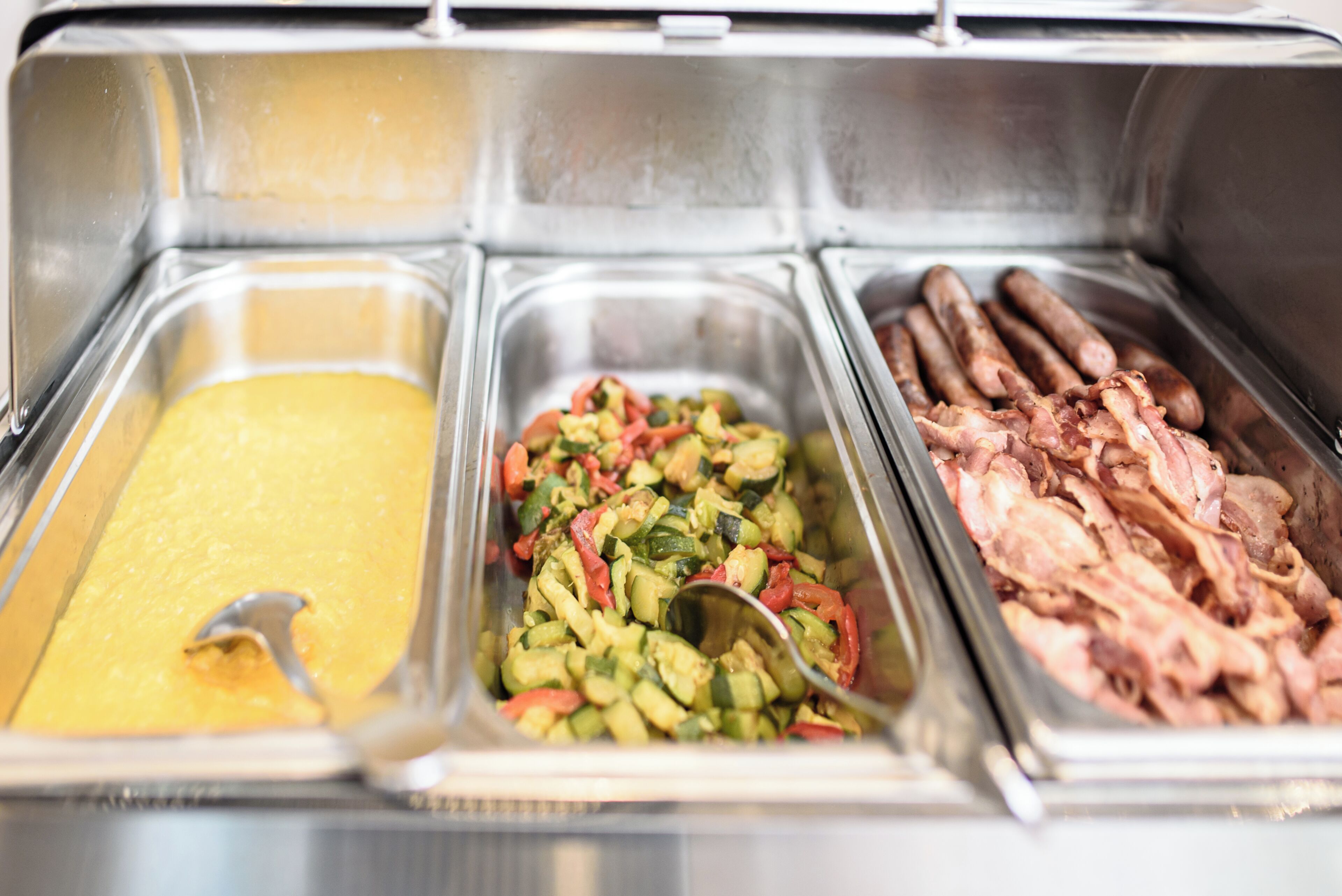 Un buffet composé de trois types de plats : une crème dessert jaune, une salade de légumes et du bacon.