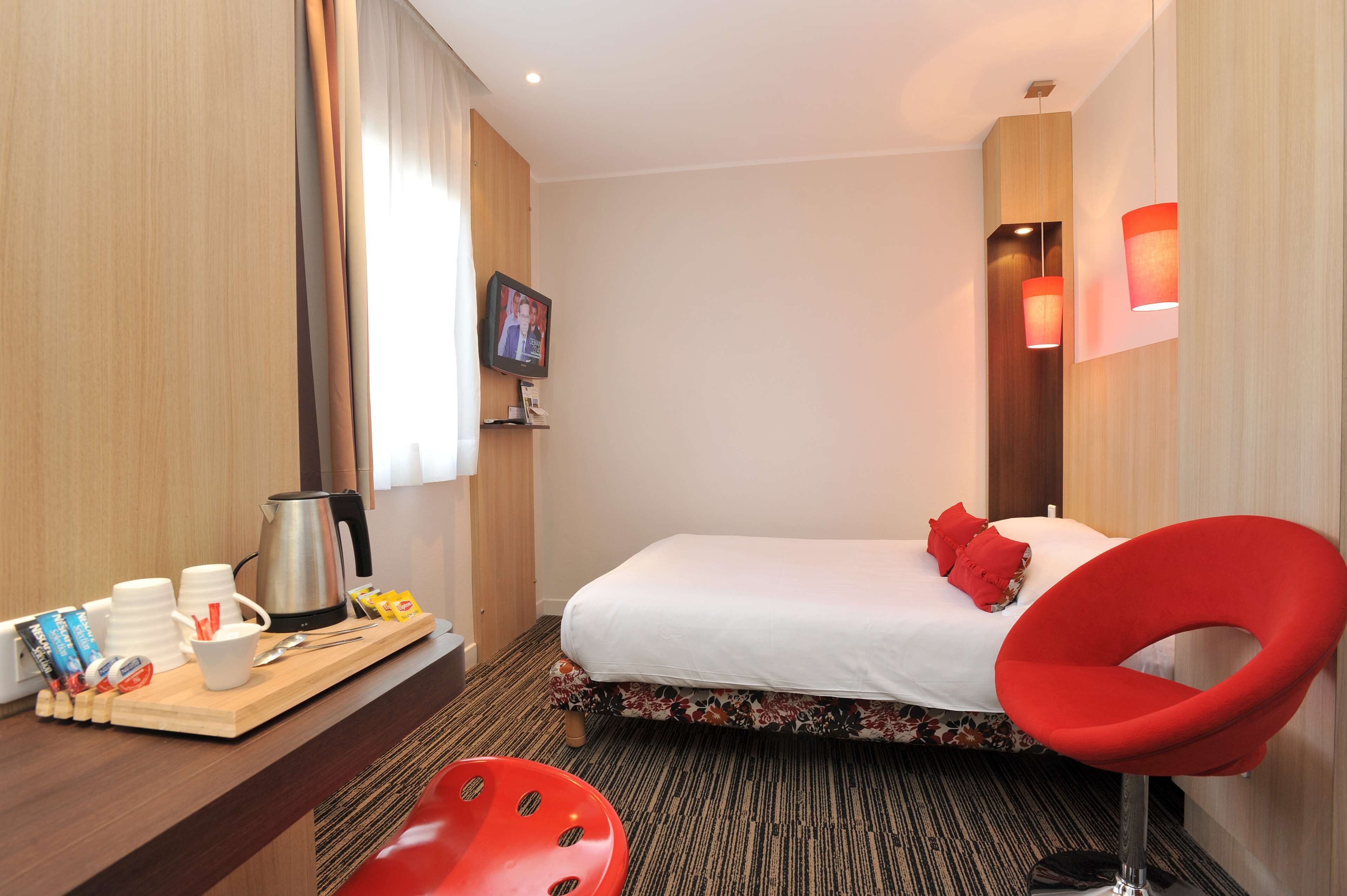 Habitación de hotel con cama, una silla roja, un escritorio de madera con una bandeja de alimentos para el desayuno y un televisor en la pared.