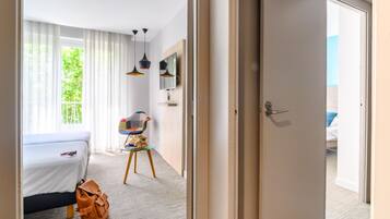 A hotel room with a bed, a desk, a chair, a table, and a door leading to another room.