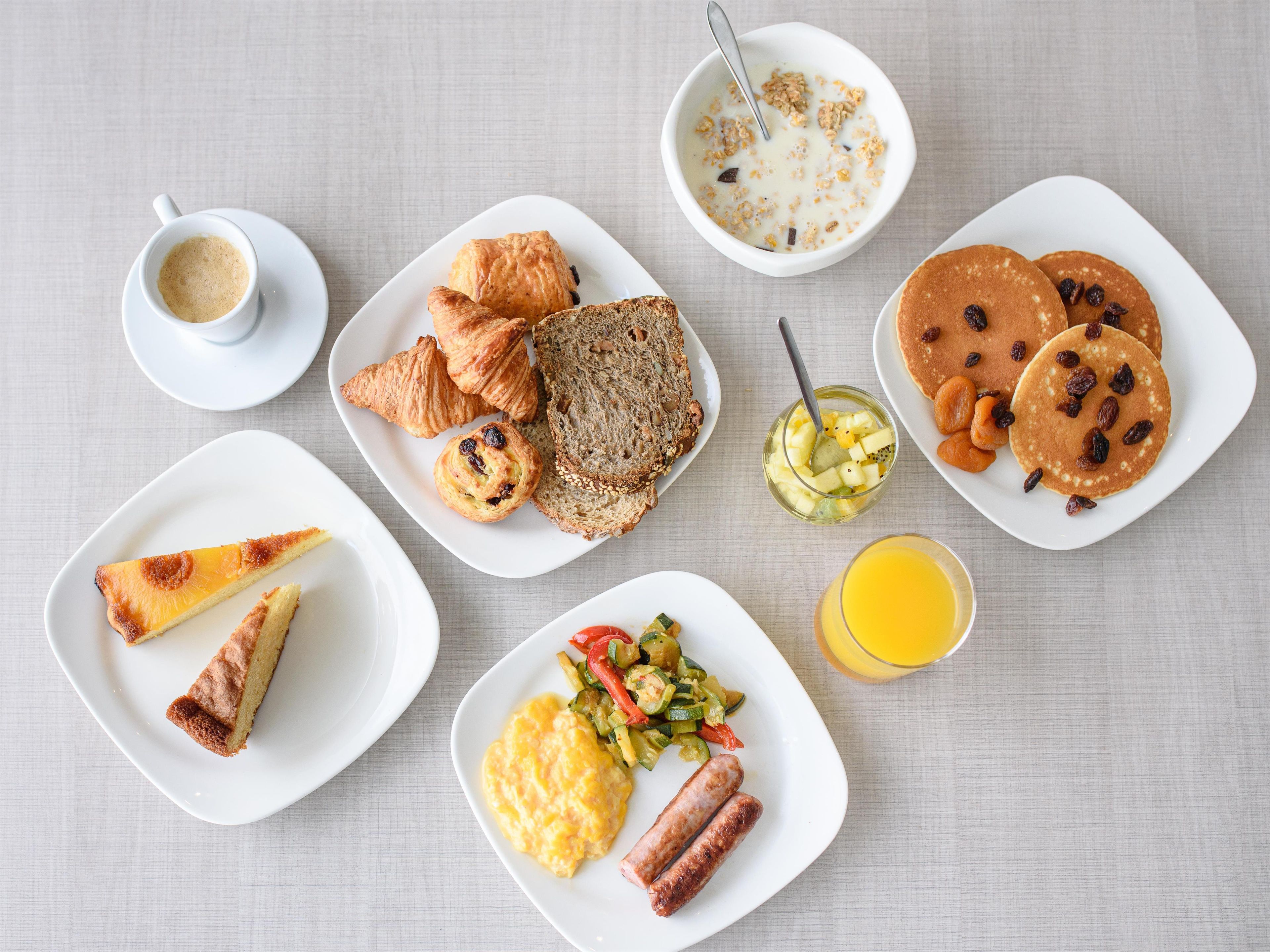 A breakfast setting with various food items on plates, including croissants, pancakes, and sausages.