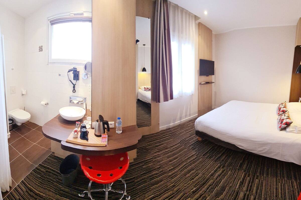 Een hotelkamer met een bed, een bureau met toiletartikelen, een wastafel en een douche.