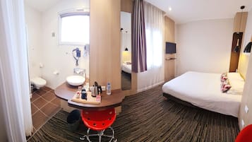 A hotel room with a bed, a desk with toiletries, a sink, and a shower.