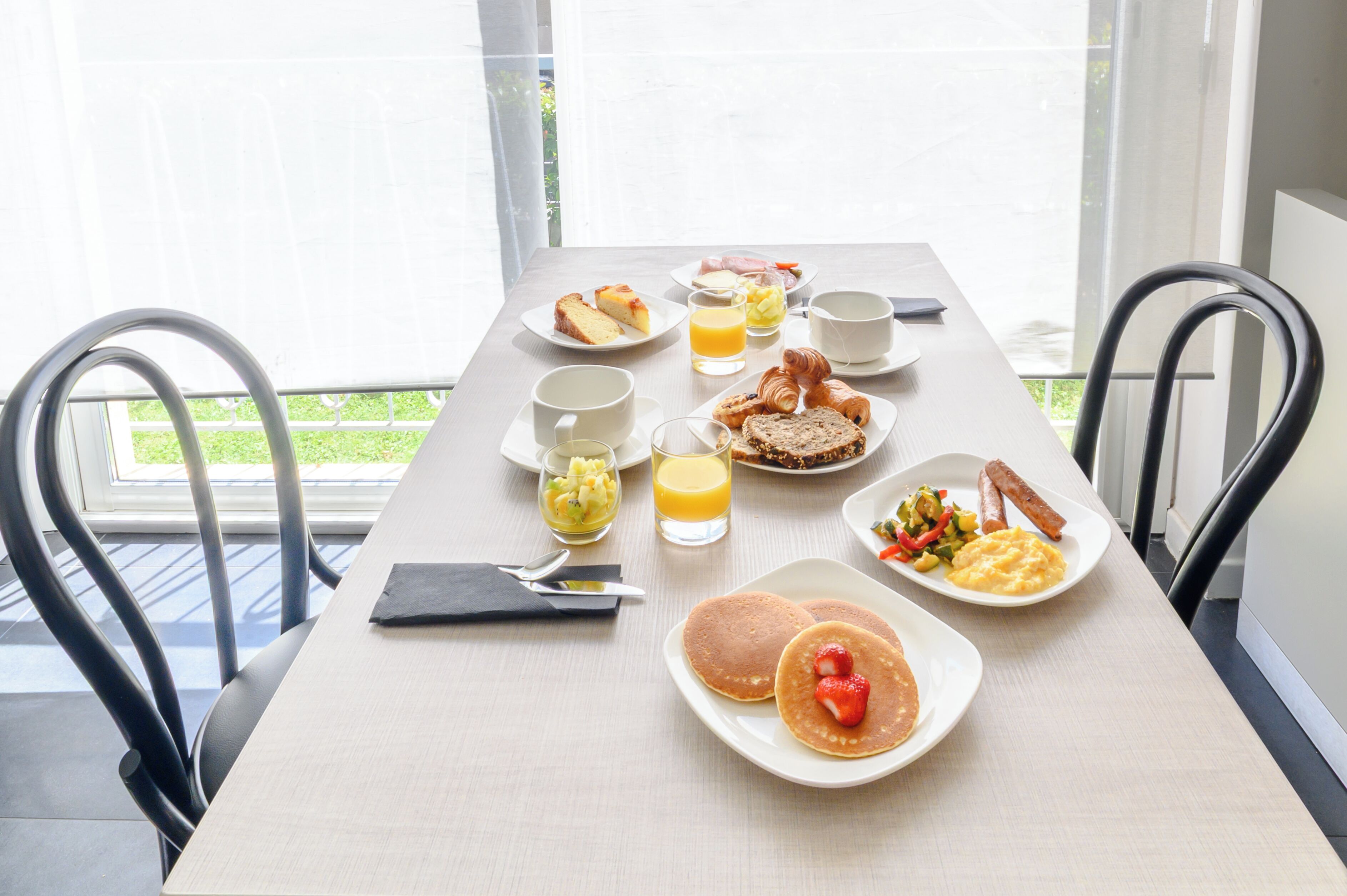 Una mesa de desayuno con platos de comida, vasos de jugo y cubiertos.