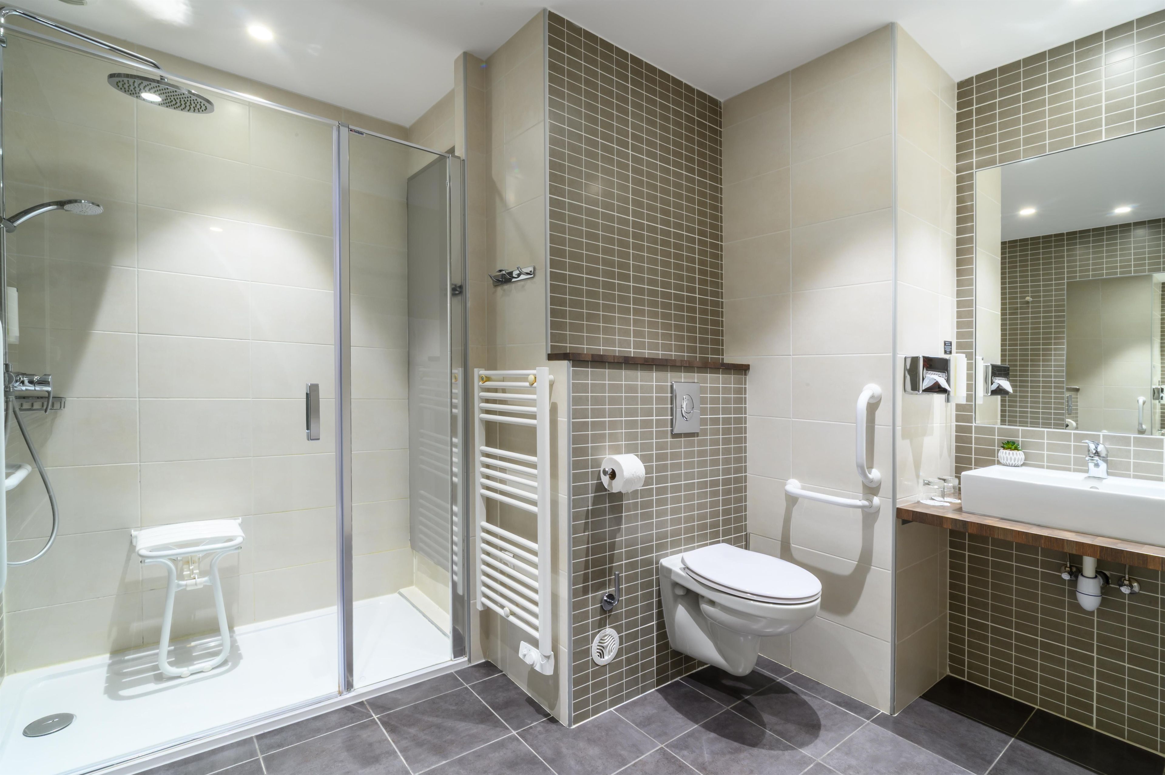 Un baño moderno con cabina de ducha de vidrio, inodoro blanco, lavabo con espejo y toallero.