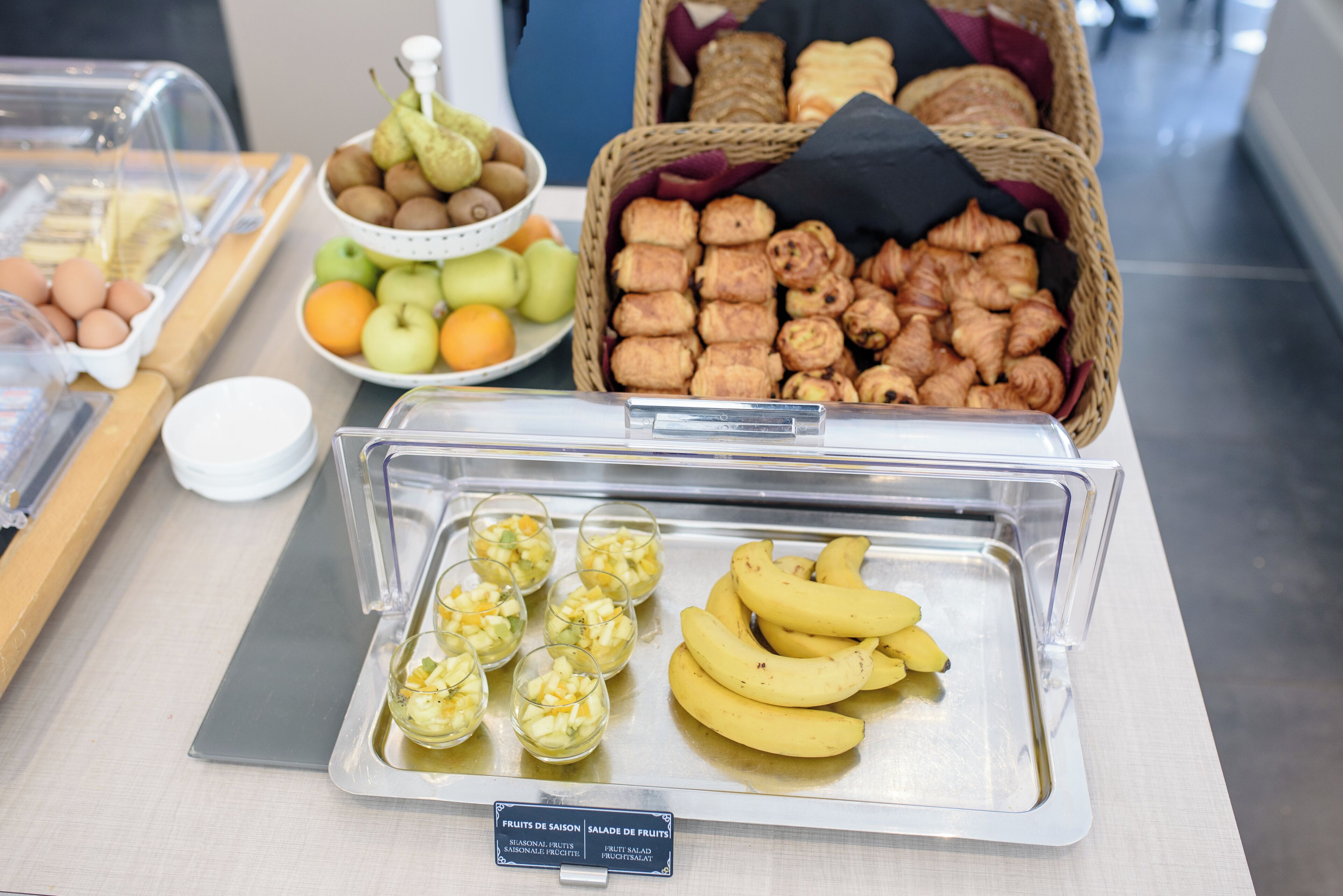 A buffet with various food items including fruits, pastries, and a sign indicating seasonal fruits and fruit salad.
