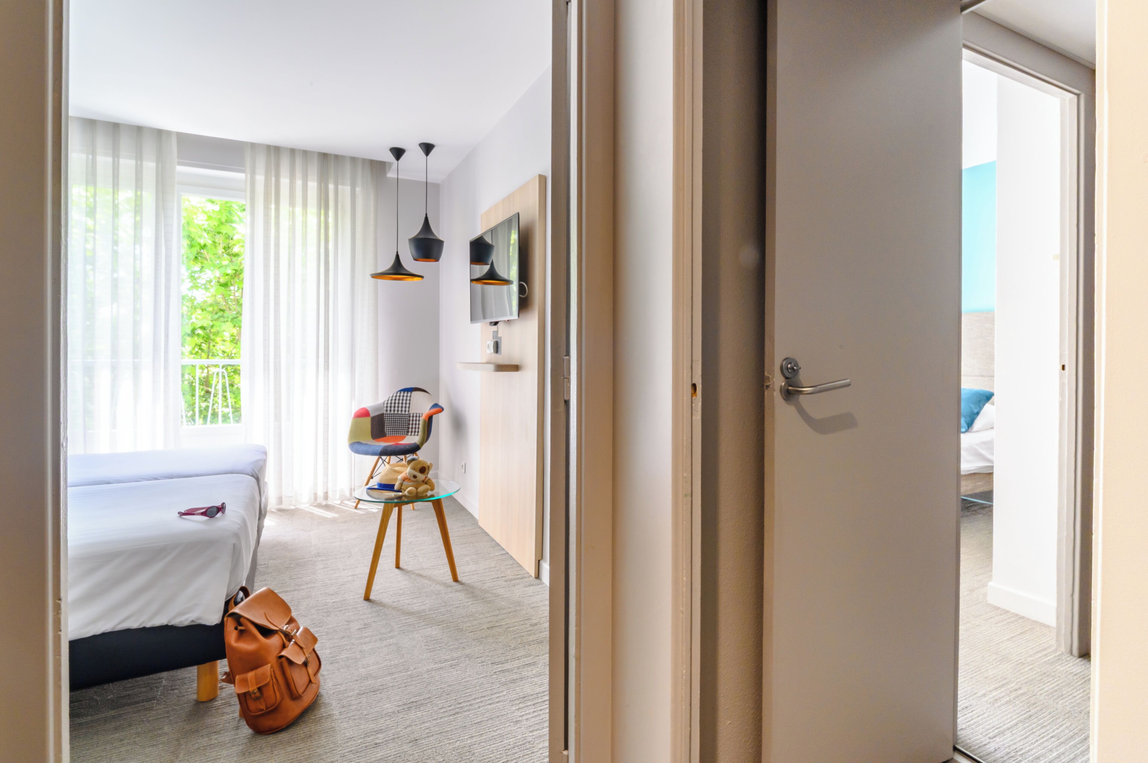 A hotel room with a bed, a small table with a chair, a television, and a door leading to a balcony.