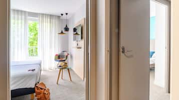 A hotel room with a bed, a small table with a chair, a television, and a door leading to a balcony.
