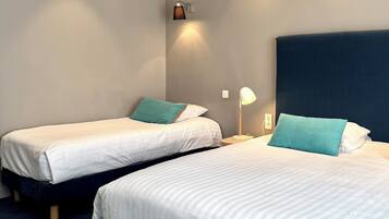 Et hotelværelse med to senge, et natbord, en lampe og en vægmonteret lysarmatur.