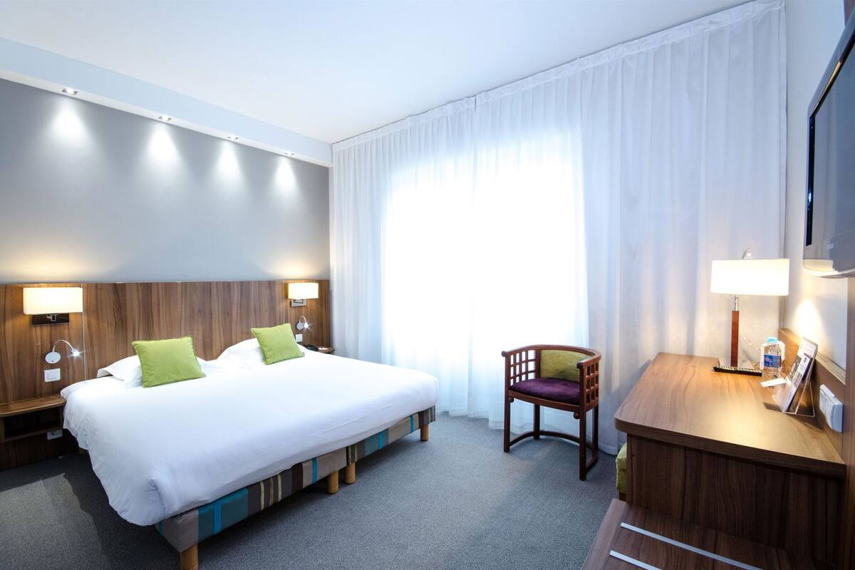 Een hotelkamer met een groot bed, bedlampen, een stoel, een bureau en een televisie.